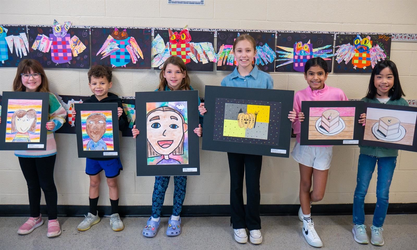 Students smile and hold pieces of art